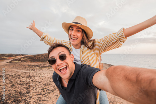 Photos Young couple on a playful piggyback ride at the coast, taking a selfie and smili