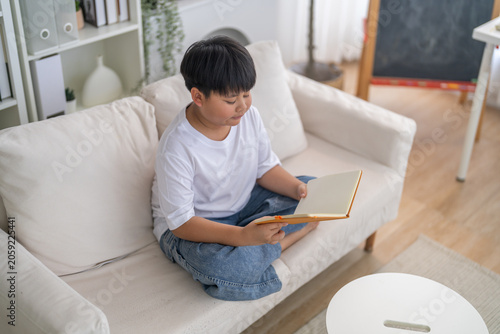 фотографія Exam preparation, Asian little boy reading and flipping through notebook pages a