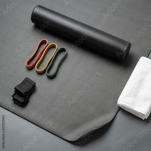 Yoga mat displays a foam roller, colorful resistance bands, ankle weights, and a towel laid out for a workout.