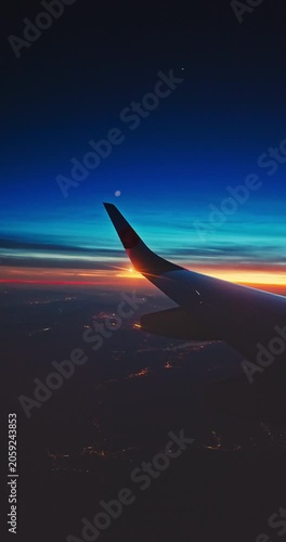 Airplane fly in sunset sky over earth of city light and wing of plane. View from the window of the Aircraft. Traveling in air.
