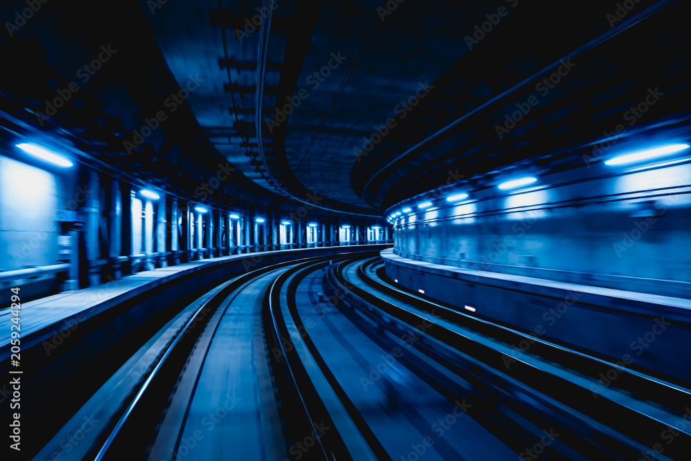 Fototapeta premium An empty curved underground subway tunnel with metal tracks and blue linear lighting along both walls.