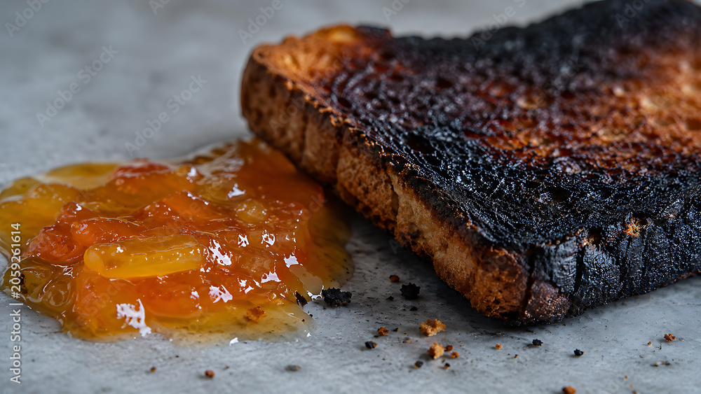 Fototapeta premium Burnt bread slice placed next to a dollop of orange marmalade sauce with marmalade breakfast overcooked blackened breadslice culinary homemade nutrition burntbread textured