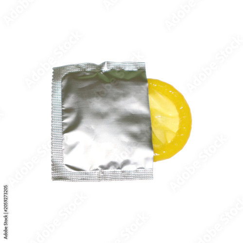 Yellow latex condom partially unwrapped from foil packaging during studio lighting for safe intimacy concept