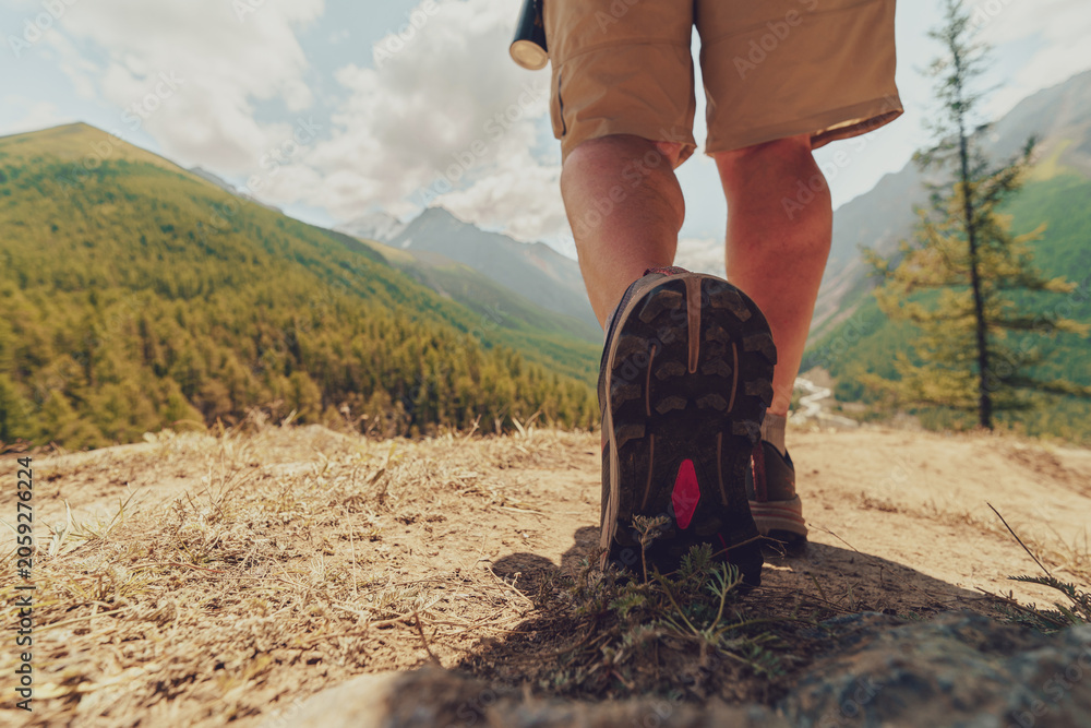 Naklejka premium low angle close up of hiker legs and boots walking on dirt trail toward green mountains and valley