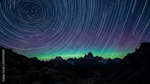 Star trails in the night sky over mountains with aurora borealis and celestial motion during twilight