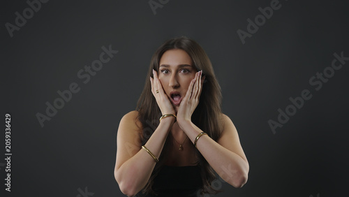 Foto Shocked woman with open mouth reacting to something surprising on dark backgroun