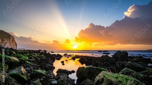 Dramatic sunset over coastal rocks and sea, with light rays bursting