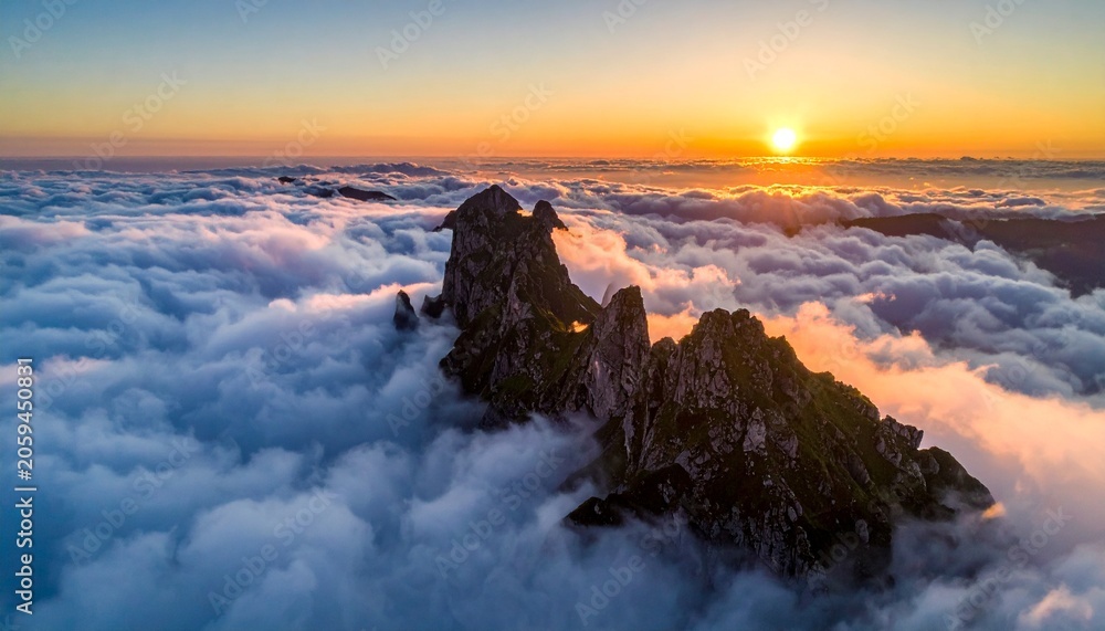 Fototapeta premium Breathtaking aerial view of rugged mountain peaks rising above a thick sea of fluffy white clouds during a beautiful golden sunrise light.