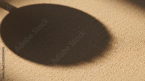 Abstract shadow of a round object with a handle cast on a textured beige surface with warm light