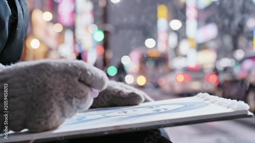 A person's hands wearing mittens hold a board on a blurry city street at night