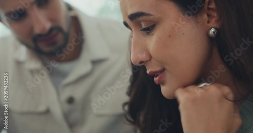 Close up young Hispanic husband comforting sad depressed wife on sofa in home living room. Mental health support, marriage couple conflict problem, grief emotion therapy, family trauma crisis concept.