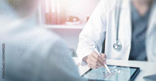 Obraz na płótnie A healthcare professional in a white coat using a tablet to explain something to a patient, highlighting the importance of technology in modern medicine
