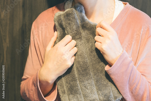 Slika na platnu woman holding a dark hot water bottle against her chest while wearing casual home clothing