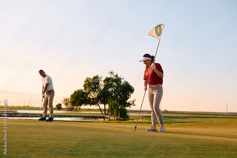 Obraz premium Couple of golfers enjoying a round of golf at sunset.