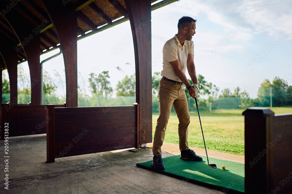 Naklejka premium Full length of a man practicing his golf swing at driving range.
