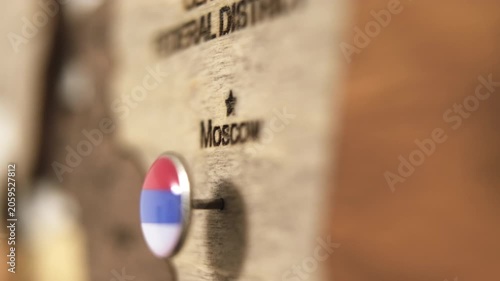 Female hand placing pin with Russian flag on Moscow on wooden map.