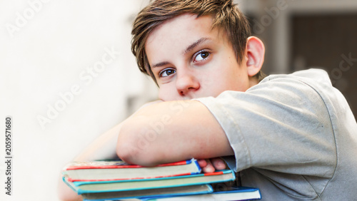 Schilderij op canvas Thoughtful teenage boy lying on a stack of books tired of studying homework