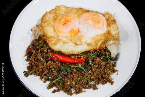 Thai stir-fried minced beef with holy basil served over rice and topped with a crispy double yolk fried egg, isolated on black background. Pad Kra Pao, famous Thai street food.