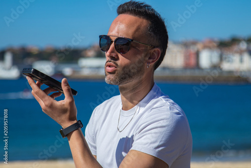 Canvastavla Casual man in white t-shirt and sunglasses sending a voice or audio message on h