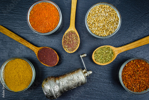 Spoons and bowls with oriental spices and spice mill on a slate board. Top view