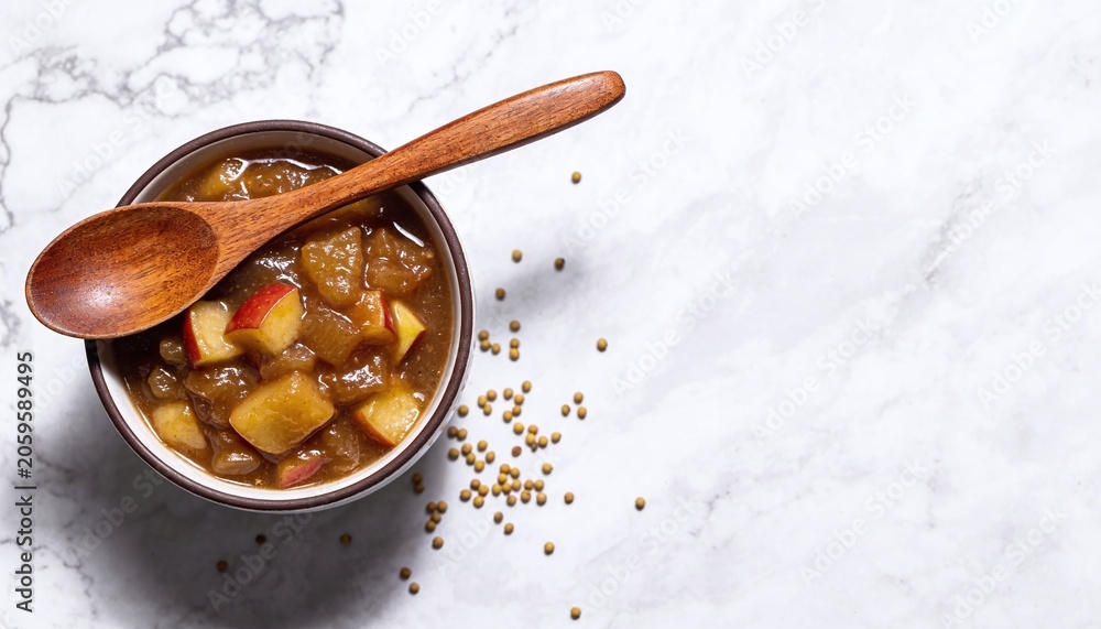 Fototapeta premium Vibrant Fruit Chutney in a Rustic Bowl with Wooden Spoon on Elegant Marble Surface, Highlighted by Scattered Spices, Warm Tones, and inviting Texture for Culinary Visuals