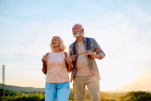 Fotografie Senior couple walking outdoors with backpacks, enjoying a healthy active lifesty