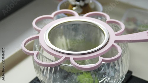4K Close up of sifting green matcha powder through cute pink flower shaped strainer into clear glass bowl on white table, Traditional tea preparation concept.