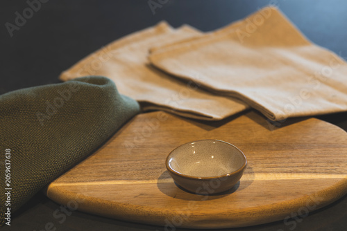 Quadro su tela Close-up of a wooden serving board styled with a small beige serving bowl, beige linen napkins, and a dark green cloth on a dark surface
