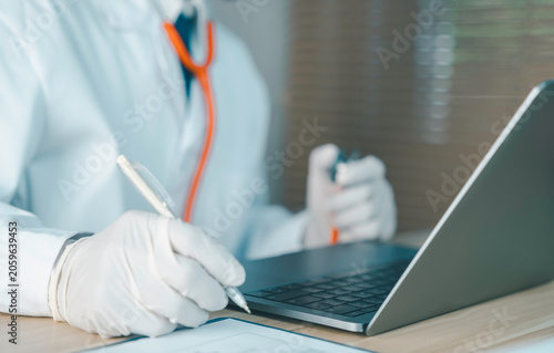 Healthcare professional wearing gloves and using a laptop while recording patient information. Concept of digital healthcare, telemedicine, electronic medical records, and clinical documentation.