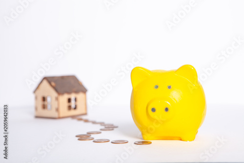 Concept of saving money for housing. Piggy bank and wooden house on white background.