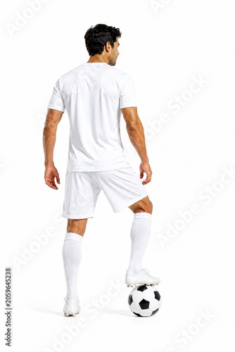 Full-length rear view of a soccer player in an all-white uniform standing with one foot resting on a football, isolated on a clean white background.