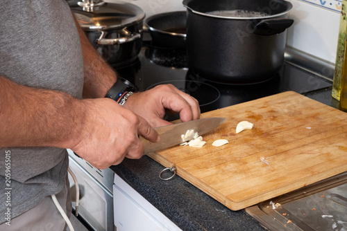Slika na platnu Man chopping garlic cloves on wooden cutting board