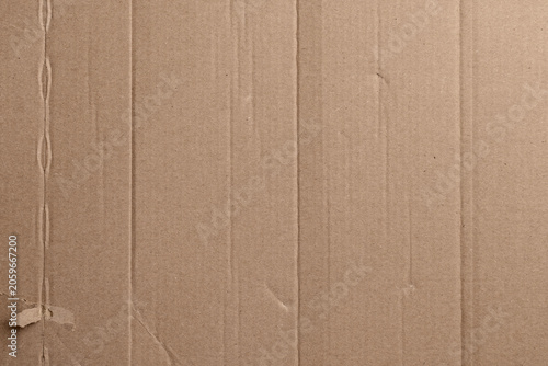 Brown cardboard texture with subtle creases and wear marks. Vertical ridges form a rhythmic pattern across the surface