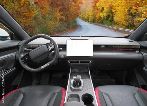 Front view of a modern car interior dashboard with blank white screen mockup facing a scenic autumn road trip view through the windshield.