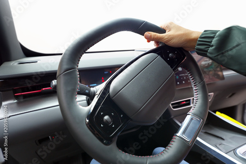 Close up of a driver hand holding a modern leather steering wheel inside a car with isolated white window mockup.