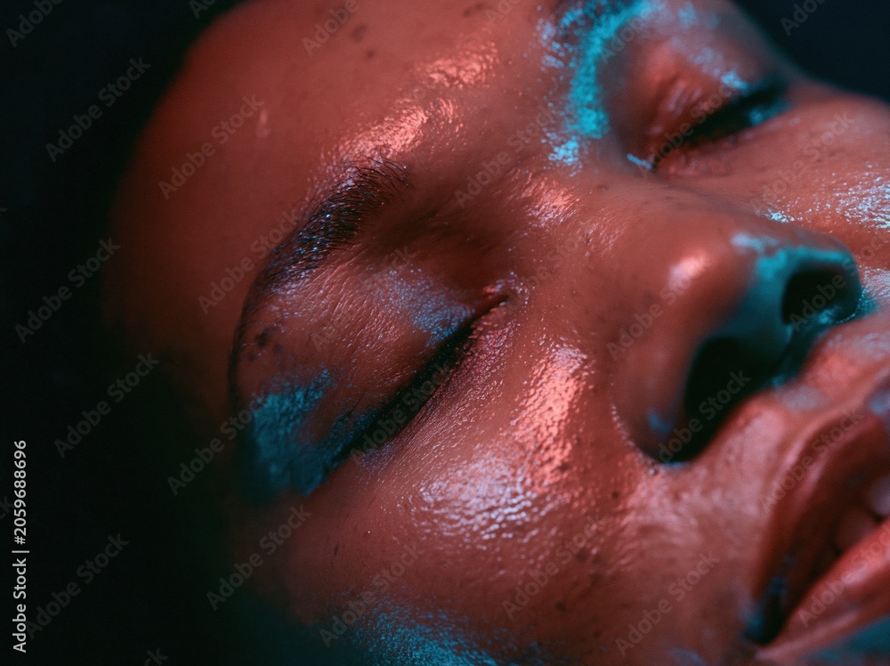 Fototapeta premium Extreme close-up of a Black woman with glowing skin under red light therapy for wellness and high-tech skincare advertising