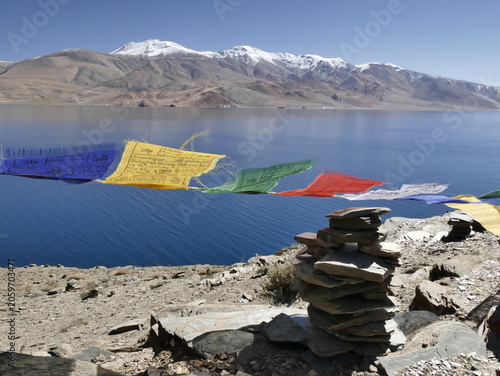 Scenic mountain lake landscape in Ladakh with tibetan prayer flags flying in the air and cairn