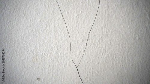 Fotografie Hairline cracks spreading on white plaster wall in a V-shape.