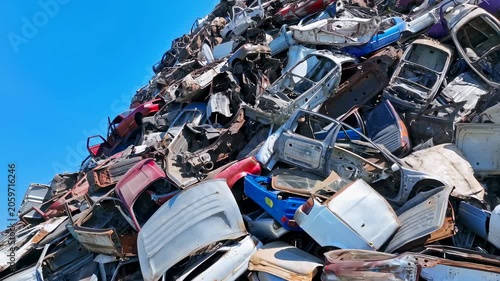 Pile of crushed and abandoned cars at a junkyard under a clear blue sky. Represents the end of vehicle life cycle and recycling industry