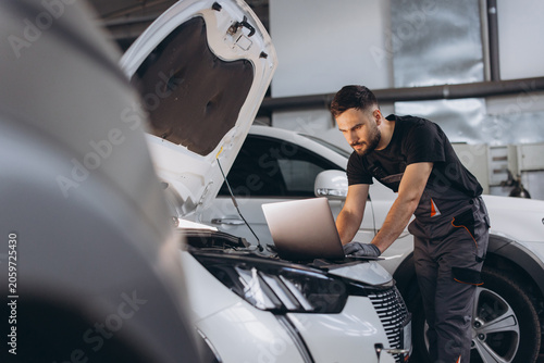 Professional male auto mechanic using a computer for diagnostic check up on a car engine in a modern garage