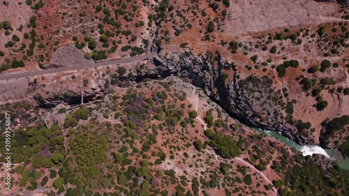 Drone footage tilting down over El Chorro's parched plateau, tracking the gorge edge as it drops to white water rapids and a jade river cutting through sun-baked scrubland below.
