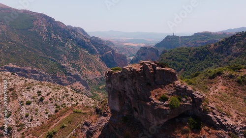 Drone footage pushing forward over a jagged mountaintop, gradually exposing the sweeping gorge basin, snaking reservoir, distant plateaus, and lone watchtower on the far ridge.