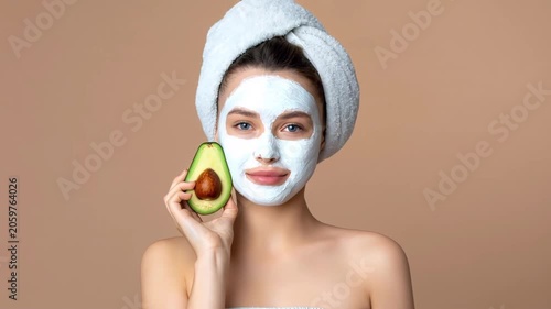 Video of young woman wearing facial mask and towel holds avocado over one eye, showcasing natural skincare, beauty care and wellness lifestyle.