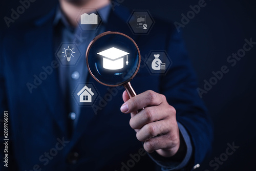 фотографія Education funding and scholarship search concept with business professional holding magnifying glass over graduation cap icon