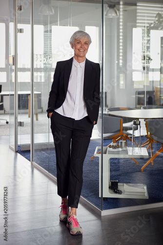 Portrait of fashionable senior businesswoman wearing pantsuit and sneakers in office