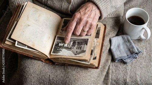 A person sits on a couch reading a vintage photo album next to a cup of coffee.