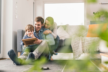 Father and son sitting on floor, using digital tablet
