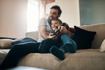 Father and son sitting together on the couch playing computer game