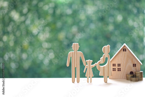 Wooden family figure set including a pregnant mother, father, and daughter standing next to a small wooden house and stacks of coins, symbolizing family growth and financial planning for a home.