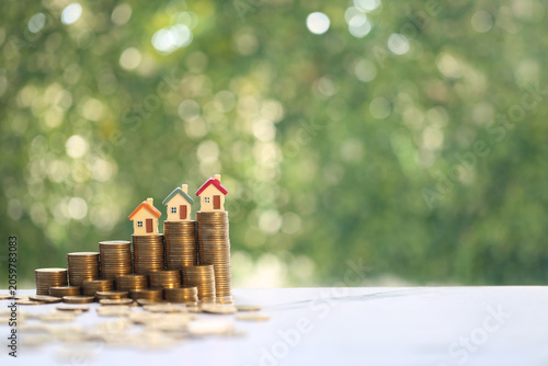 Miniature house model beside five stacks of gold coins arranged in ascending order, representing the concept of financial growth, saving money for a house and investment success.